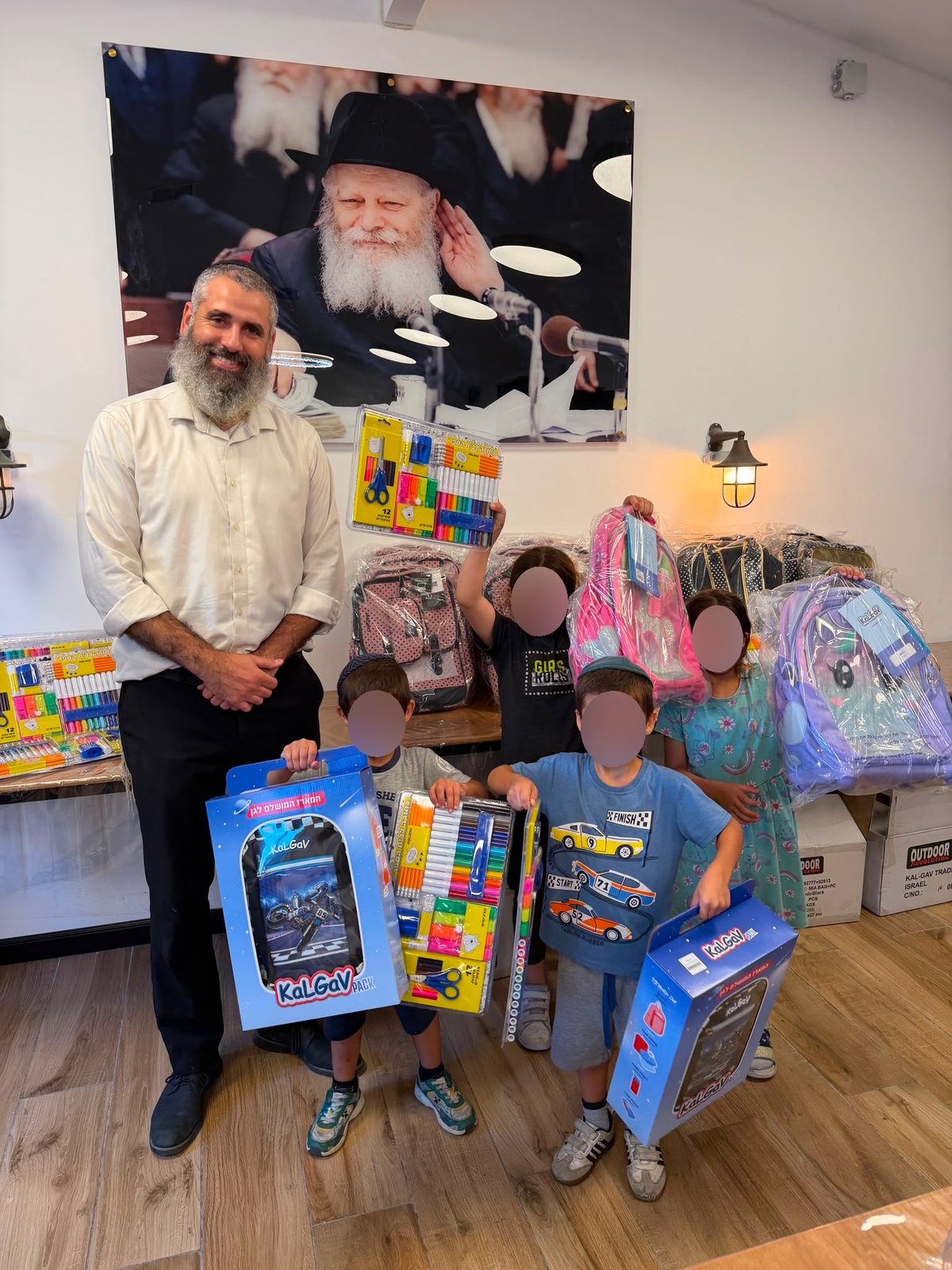 הרב עם ילדים שקיבלו ילקוטים וערכות כלי כתיבה, הפנים מטושטשים